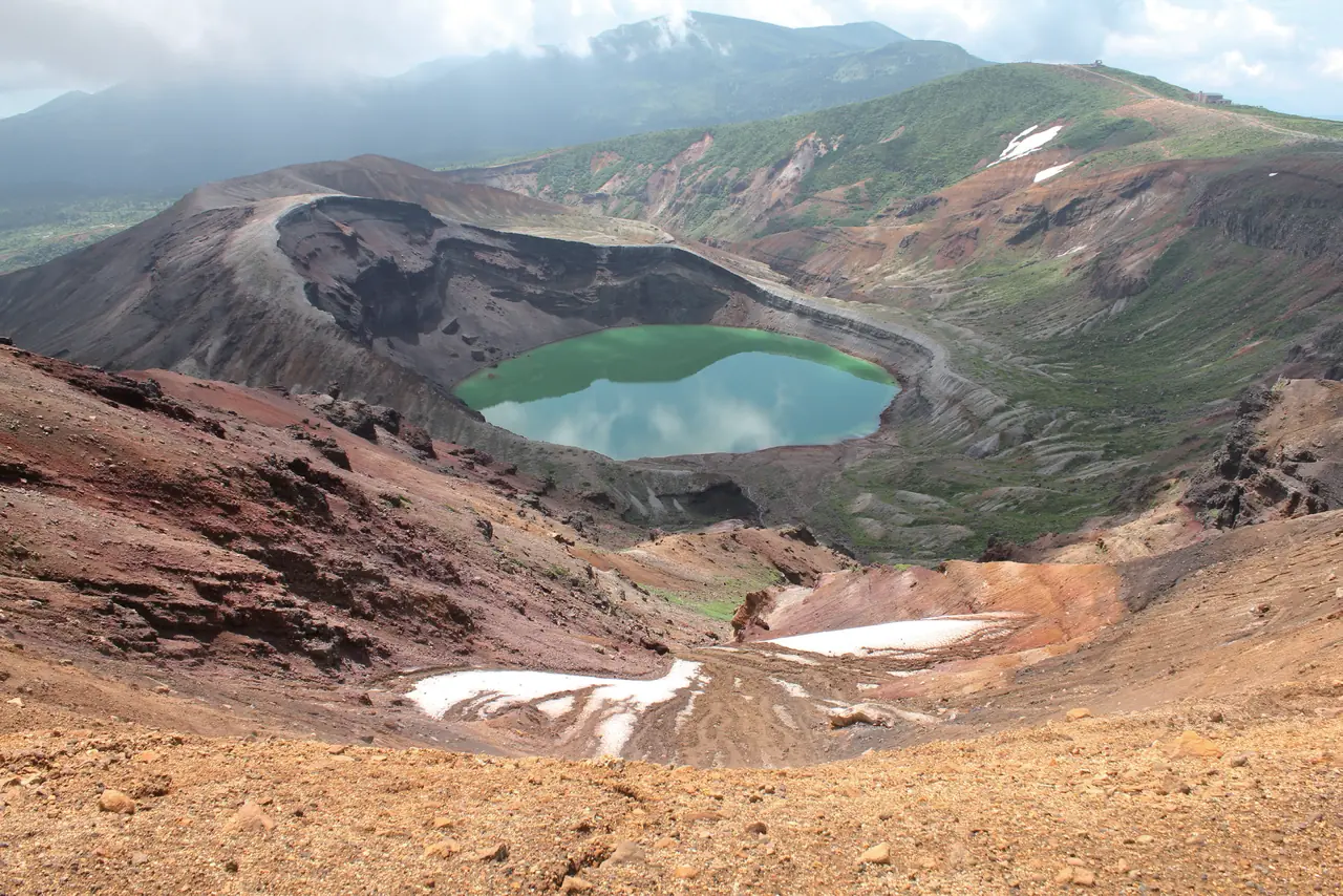 火口の底に緑色の水をたたえた御釜と、残雪のある赤茶けた山肌